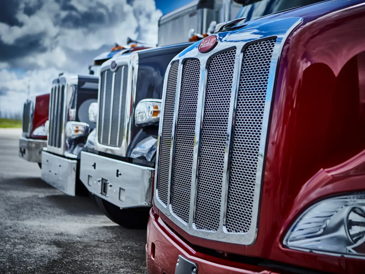 Four iconic Peterbilt grilles lined in formation, set against a moody blue sky